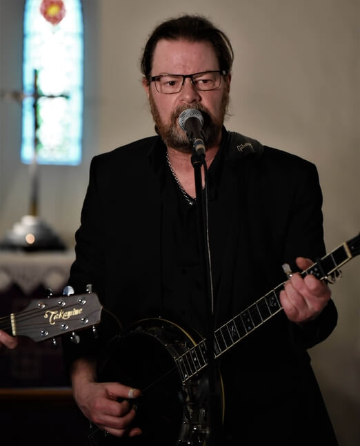 Bild på Magnus Edring sjungandes med banjo. Gospel och country.